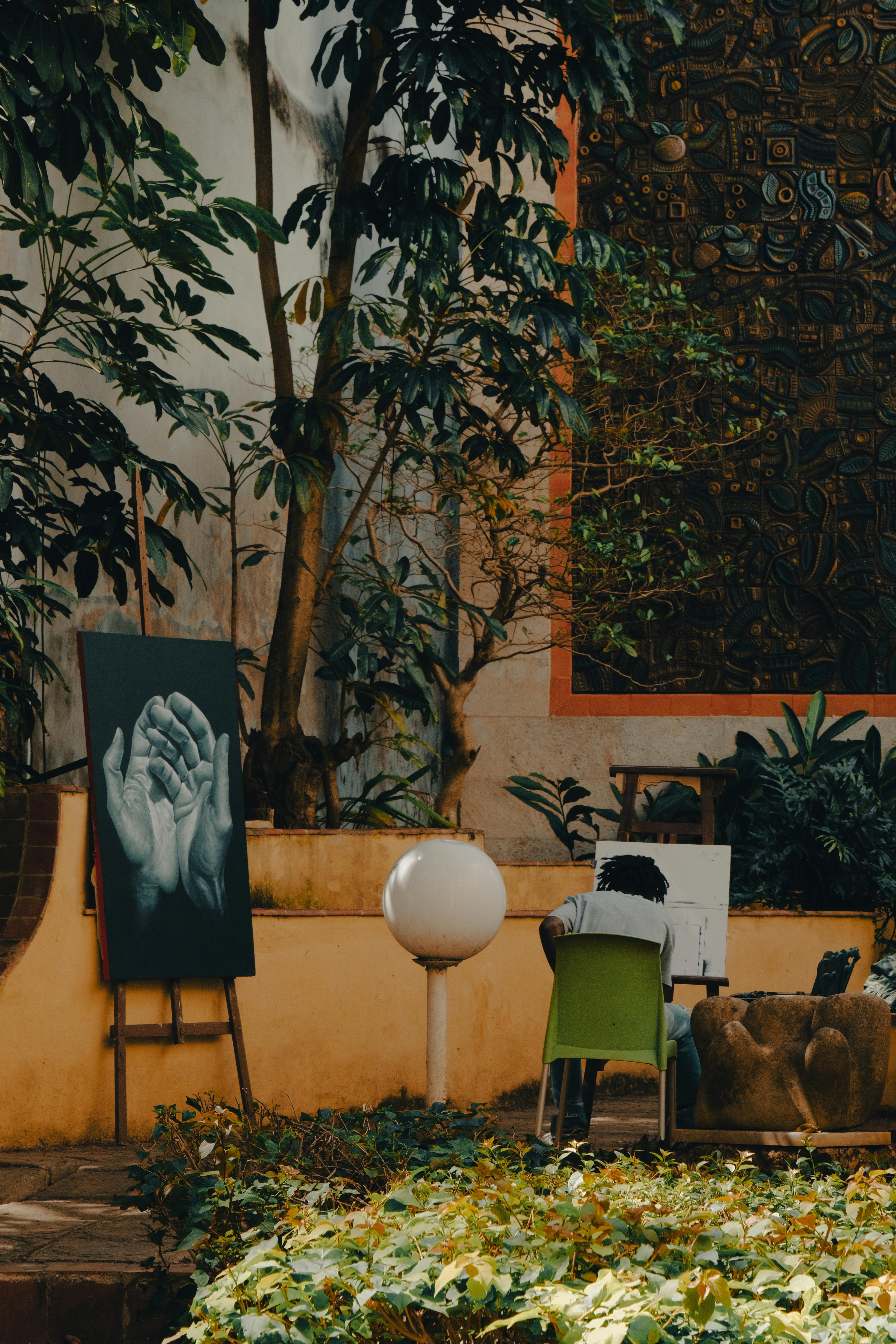 An outdoor studio with paintings, plants, and warm shadows
